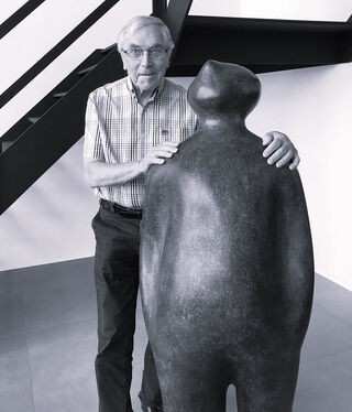 Schwarz-Weiß-Fotografie des belgischen Künstlers und Bildhauers Guido Deleu neben seiner bekannten Skulptur The Visitor.
